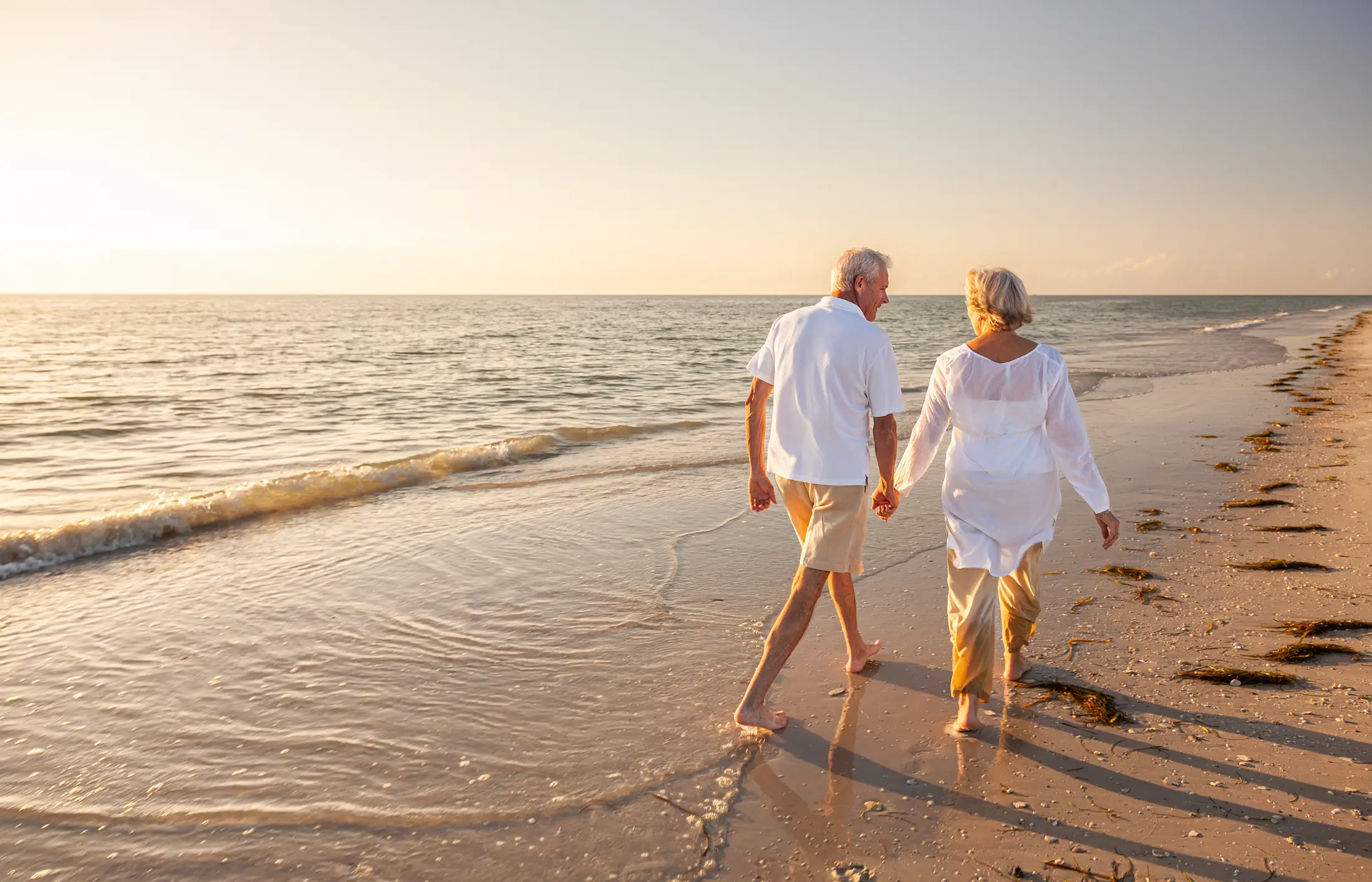 Pareja jubilada caminando de la mano por una playa de la Riviera Maya al atardecer